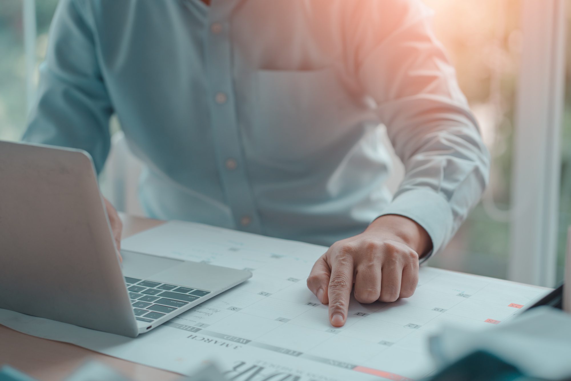business person sitting at a desk with an open laptop and calendar